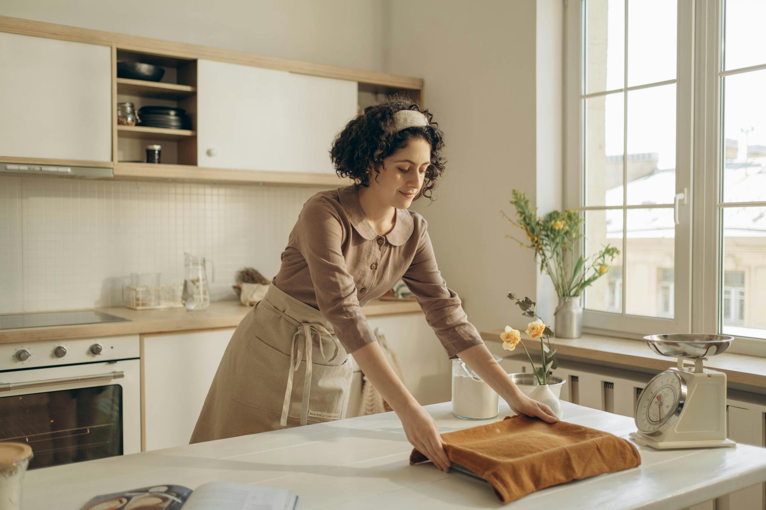 Woman with curly hair preparing dough in a bright, cozy kitchen setting.